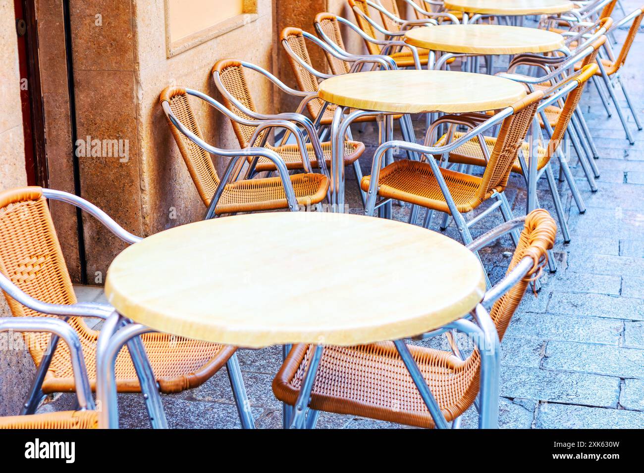 Fila di tavoli vuoti con sedie per strada. Le sedie sono fatte di legno e metallo. I tavoli sono rotondi e hanno una parte superiore bianca. Le sedie sono sistemate Foto Stock