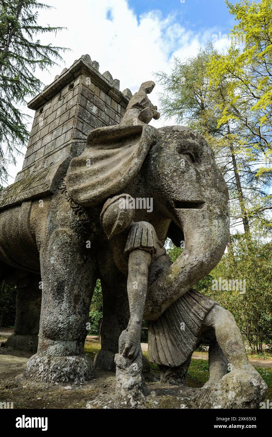 Scultura in pietra di un elefante che distrugge un soldato romano nel Sacro Bosco di Bomarzo. Questa intricata e storica statua è adagiata tra la lussureggiante Foto Stock