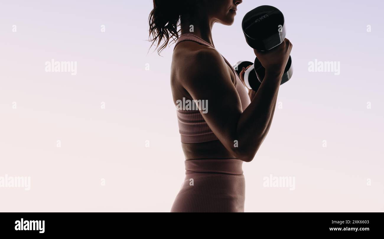 Una donna atletica che indossa l'abbigliamento sportivo svolge un allenamento completo in studio. Sagomata su uno sfondo rosa, utilizza manubri e sollevamento pesi Foto Stock