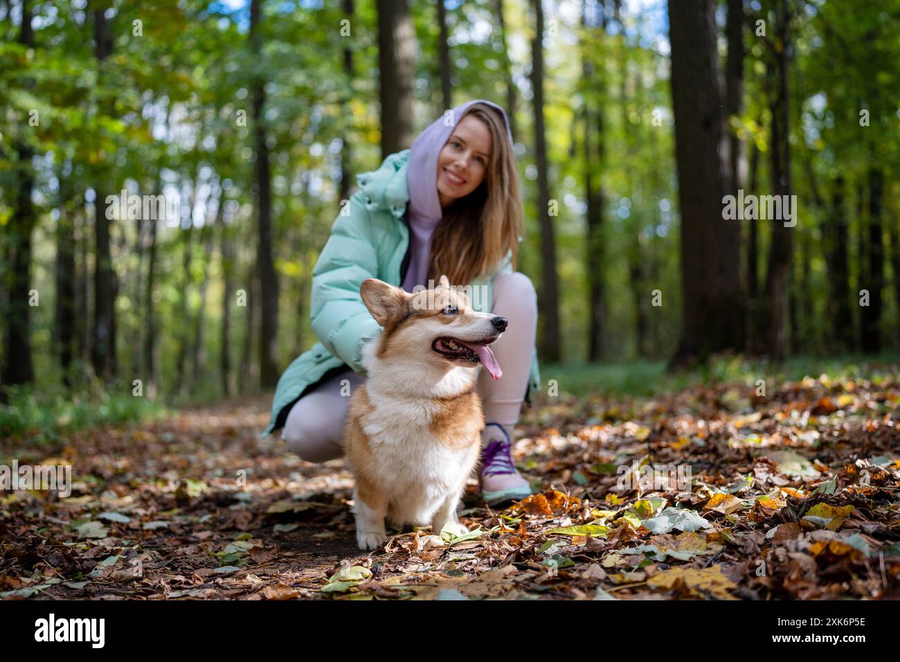 Una donna è nel parco con i suoi corgi, godendosi il giorno d'autunno e la compagnia del suo cane Foto Stock
