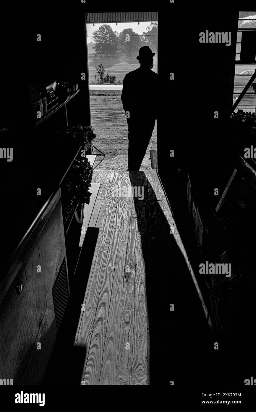 Macedonia, Arkansas, Stati Uniti – 27 giugno 2024: Foto orizzontale del proprietario del negozio appoggiato alla porta d'ingresso del negozio in silhouette davanti ad esso Foto Stock