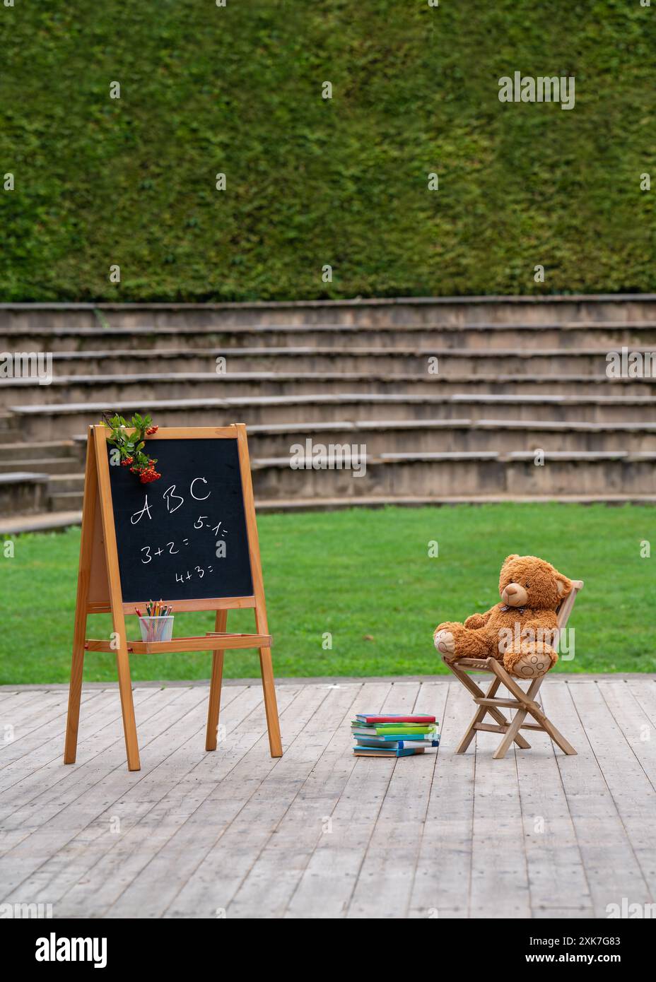 Presto torneremo a scuola. All'aria aperta c'è una tavola di legno con iscrizioni, e un orsacchiotto giallo siede su una piccola sedia. Ci sono libri nelle vicinanze. Foto Stock