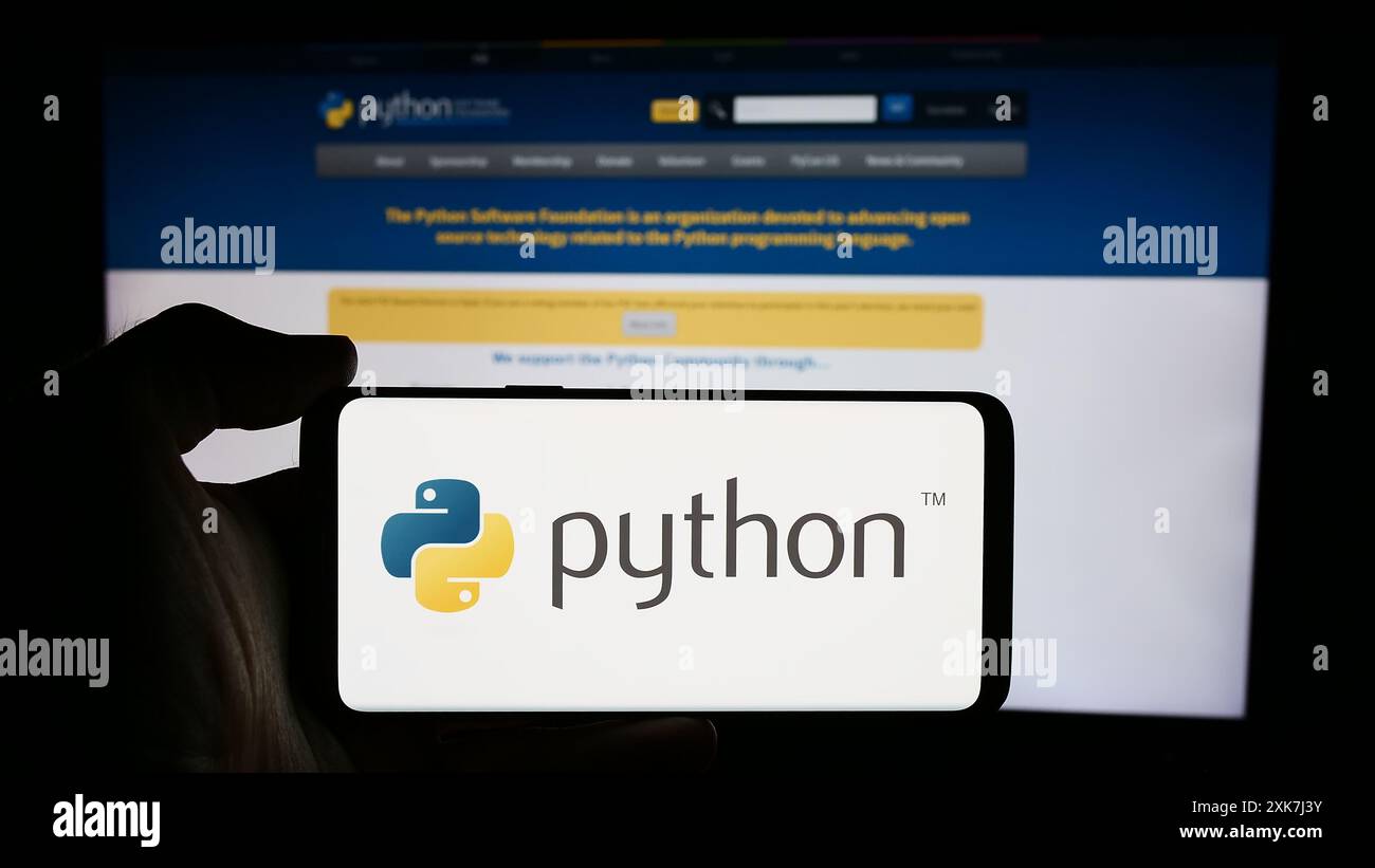 Persona che detiene un cellulare con il logo dell'organizzazione Python software Foundation (PSF) davanti alla pagina Web. Mettere a fuoco il display del telefono. Foto Stock