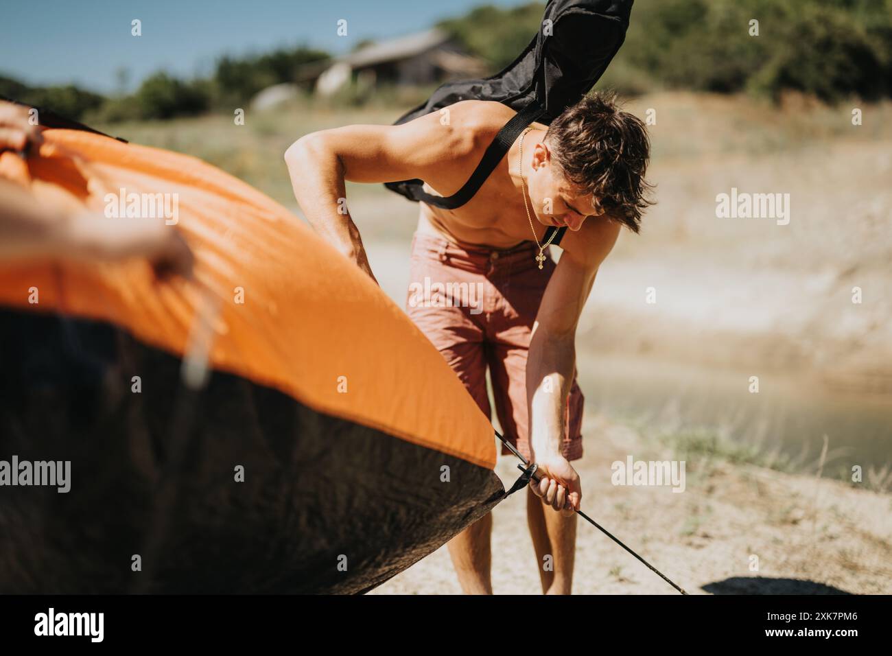Un giovane che prepara una tenda in un campeggio sul lago in una giornata di sole Foto Stock