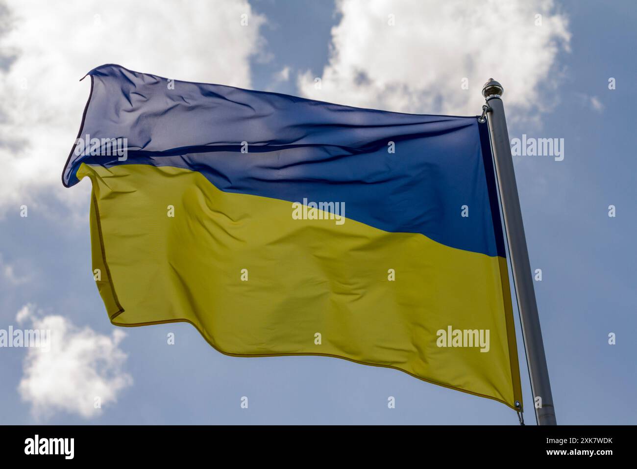 Bandiera dell'Ucraina che sventola nel vento sulla pala contro il cielo con nuvole nella giornata di sole, primo piano Foto Stock