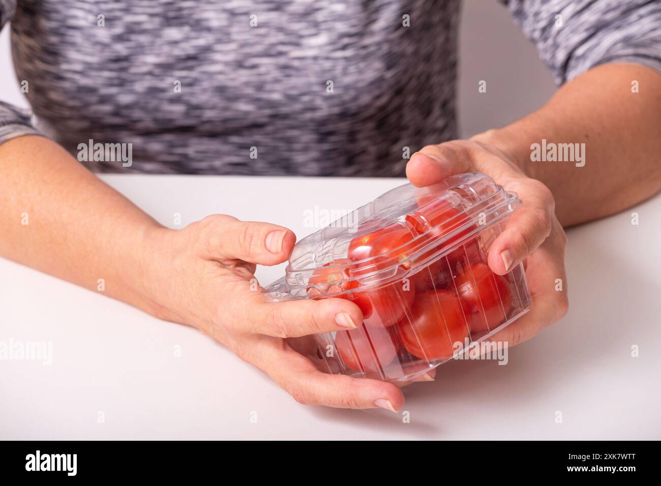 Pomodori ciliegini in scatola di plastica. Donna che tiene piccoli pomodori in un imballaggio trasparente, primo piano con messa a fuoco selettiva Foto Stock