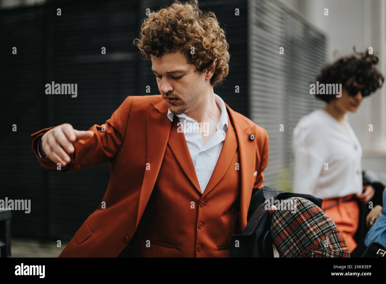 Giovane professionista con elegante tuta arancione che adatta la sua giacca all'aperto Foto Stock
