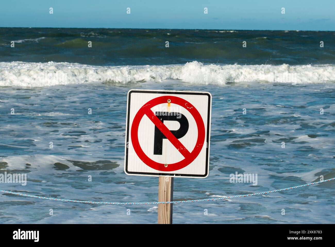 Un segno quadrato bianco con un cerchio rotondo rosso e la lettera p con vernice nera. La segnaletica e' su un palo di legno con l'oceano sullo sfondo. Foto Stock