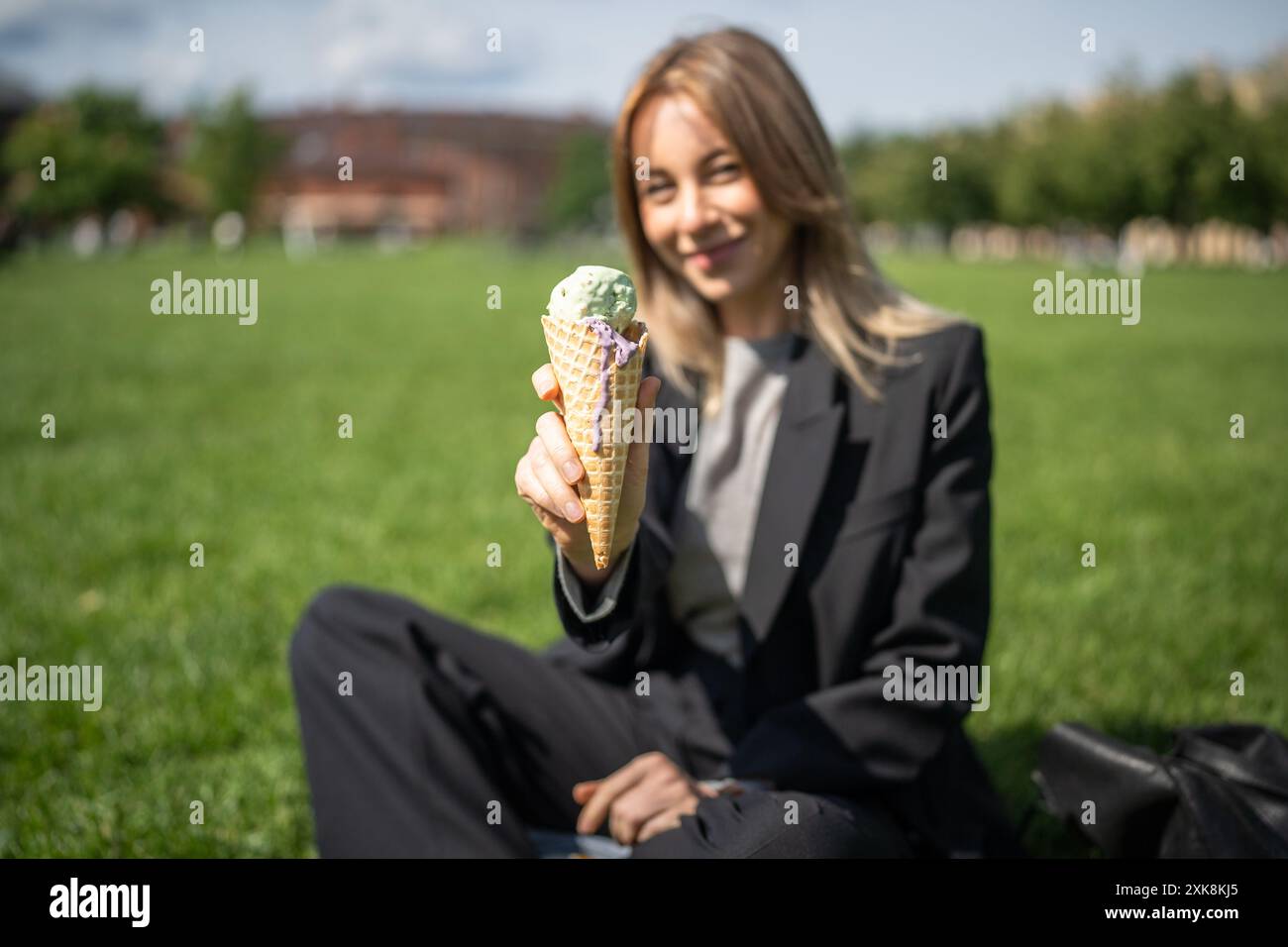 Delizioso gelato verde in cono di cialde tenuto da una donna in un ambiente sfocato nel verde del parco durante il caldo estivo Foto Stock