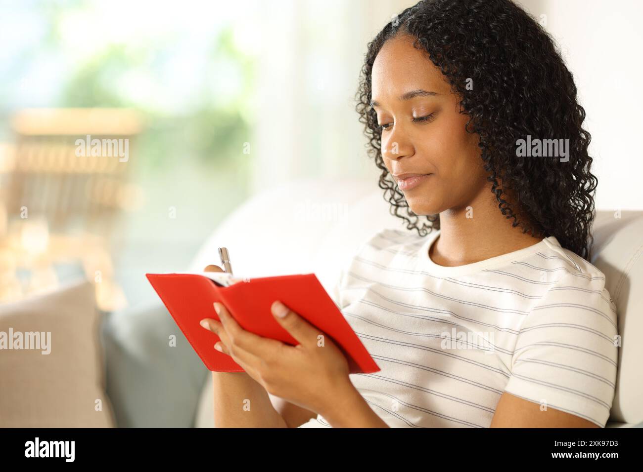 Donna nera seria che scrive in agenda rossa a casa Foto Stock