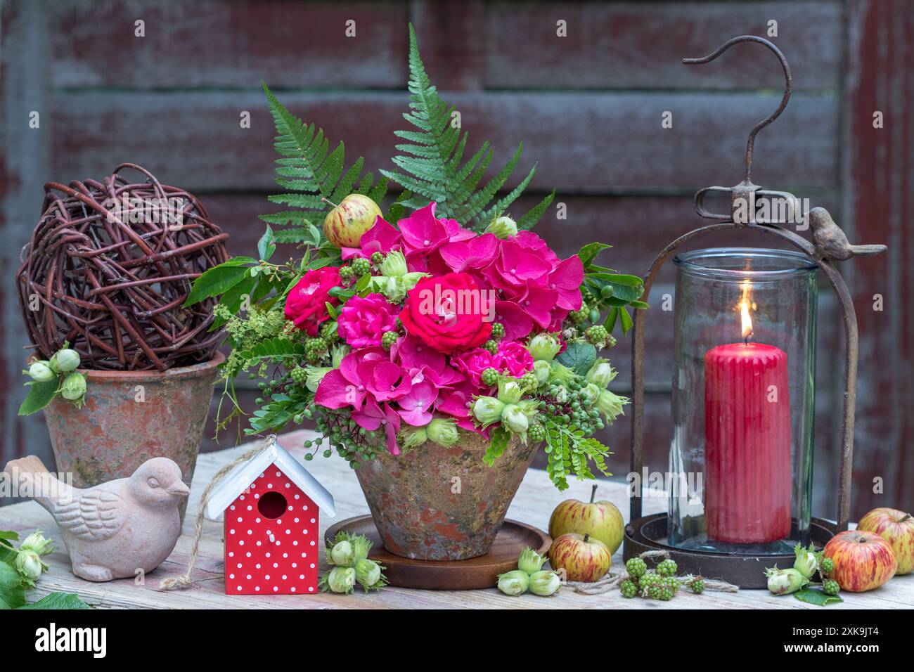 sistemazione in giardino con fiori con rose rosa, ortensie in fiore, nocciole, more e foglie in una pentola di terracotta e lan vintage Foto Stock