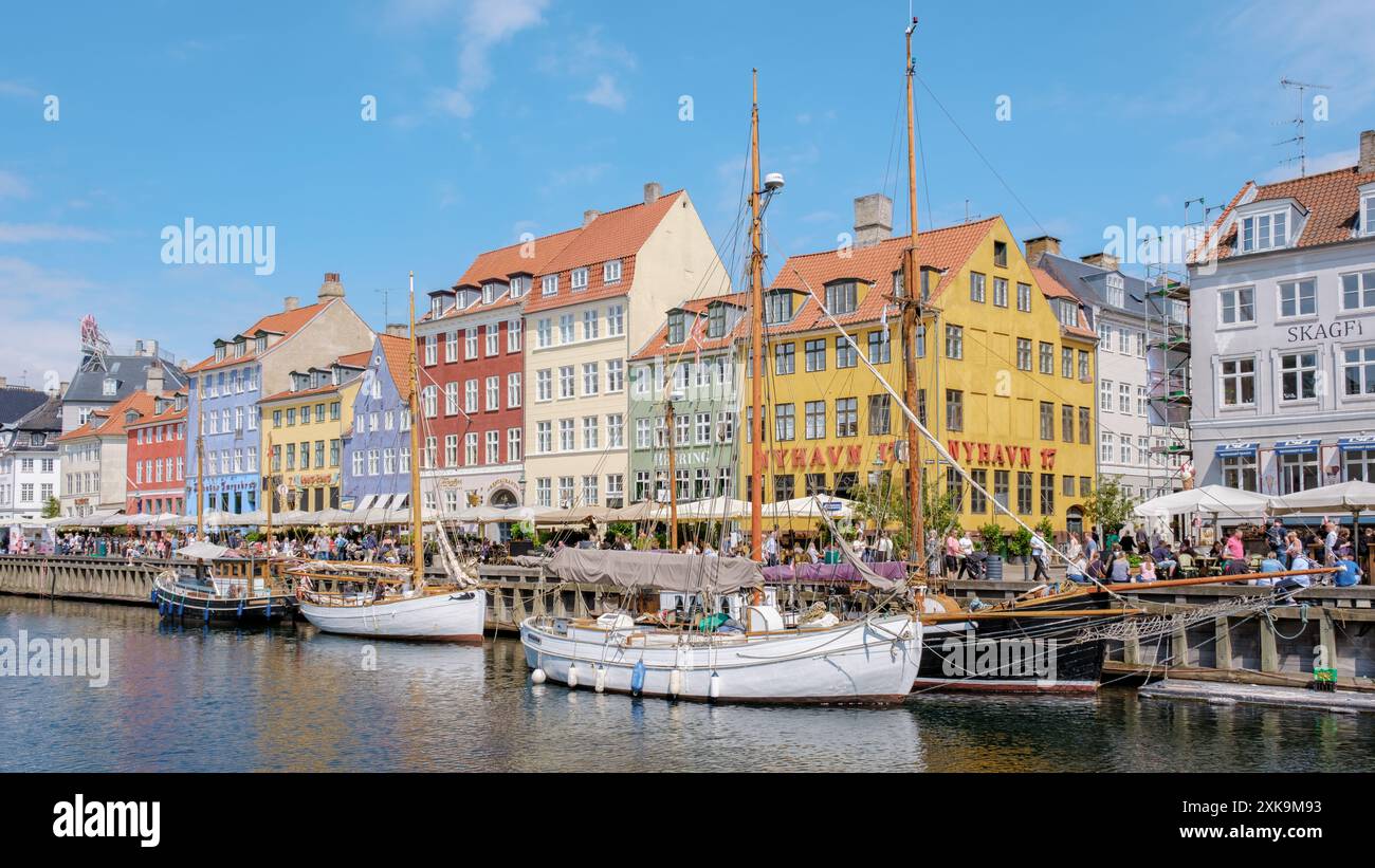 Copenaghen Danimarca 21 luglio 2024, Una giornata di sole a Nyhavn di Copenaghen, con edifici dai colori vivaci che costeggiano il lungomare. Le barche a vela sono attraccate e la gente passeggiava lungo le strade acciottolate. Foto Stock