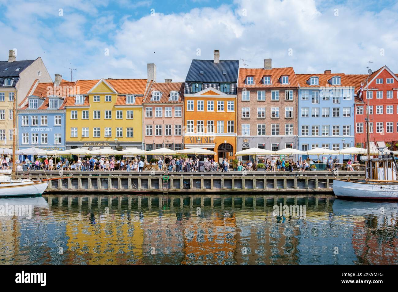 Copenaghen Danimarca 21 luglio 2024, Una vivace scena sul lungomare di Copenaghen, Danimarca, con edifici colorati, caffetterie e barche. Foto Stock