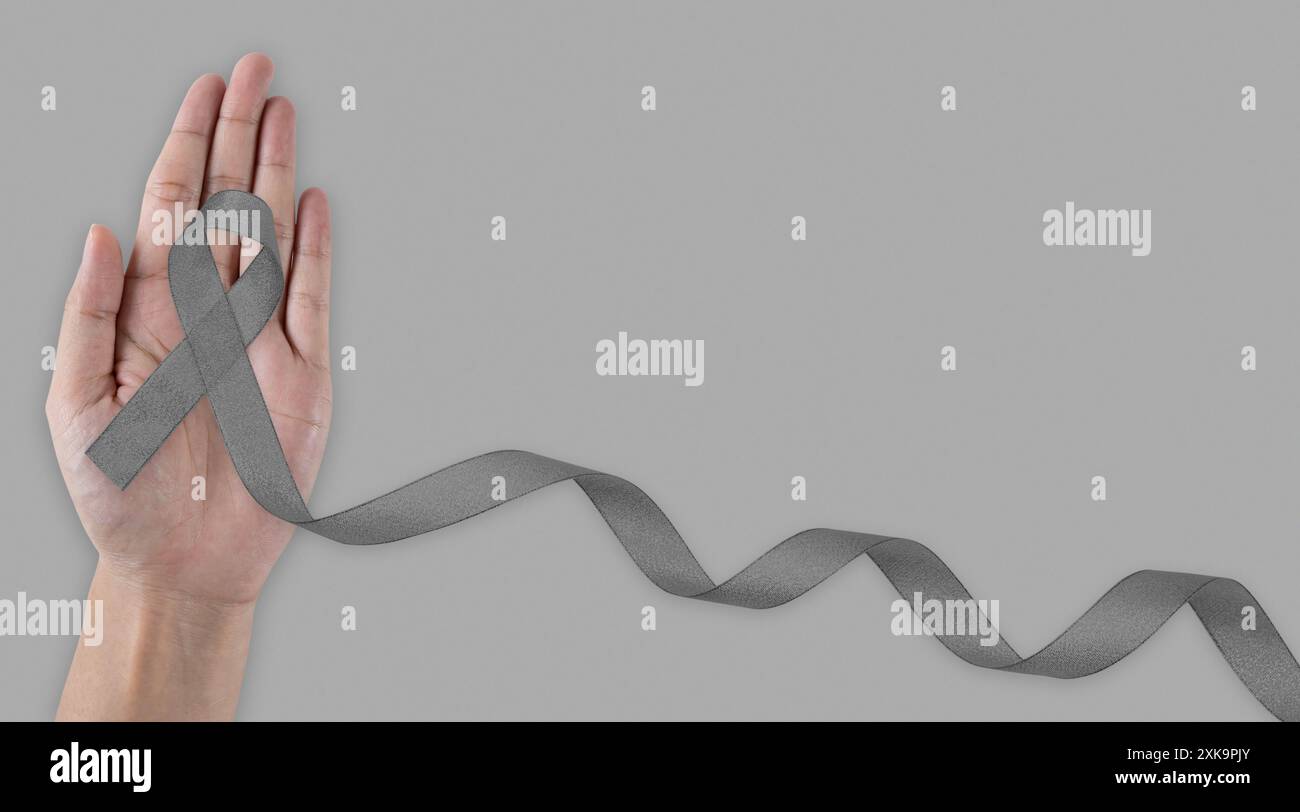 Il concetto di giornata mondiale del cancro e della sanità. Brain Cancer Awareness Month, donna mano che tiene il nastro di colore grigio per sostenere le persone che vivono. Foto Stock