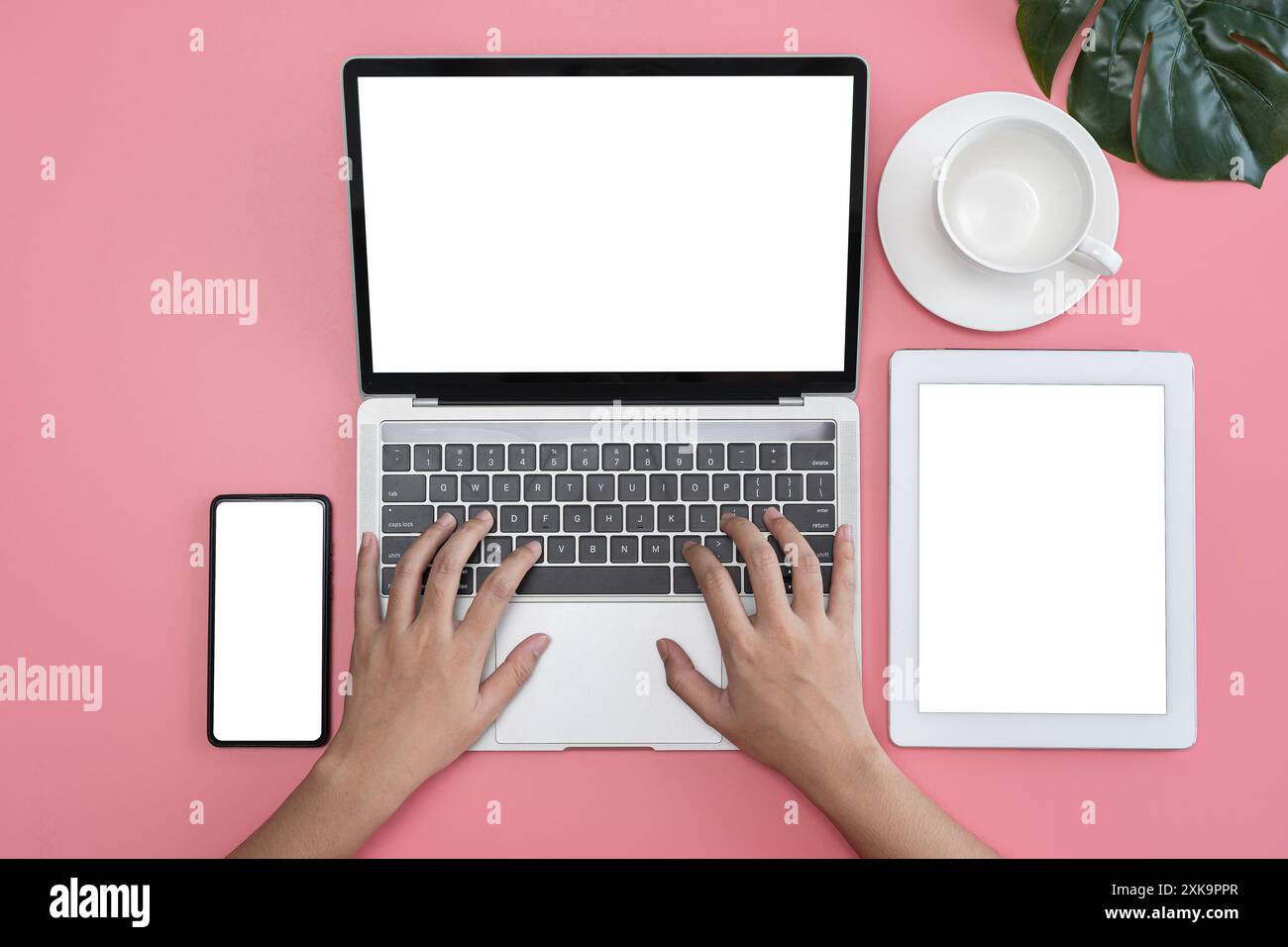 Vista dalla scrivania rosa pastello. Donna che utilizza laptop, smartphone e schermo tablet, tazza di caffè. Spazio vuoto per scopi pubblicitari. Foto Stock