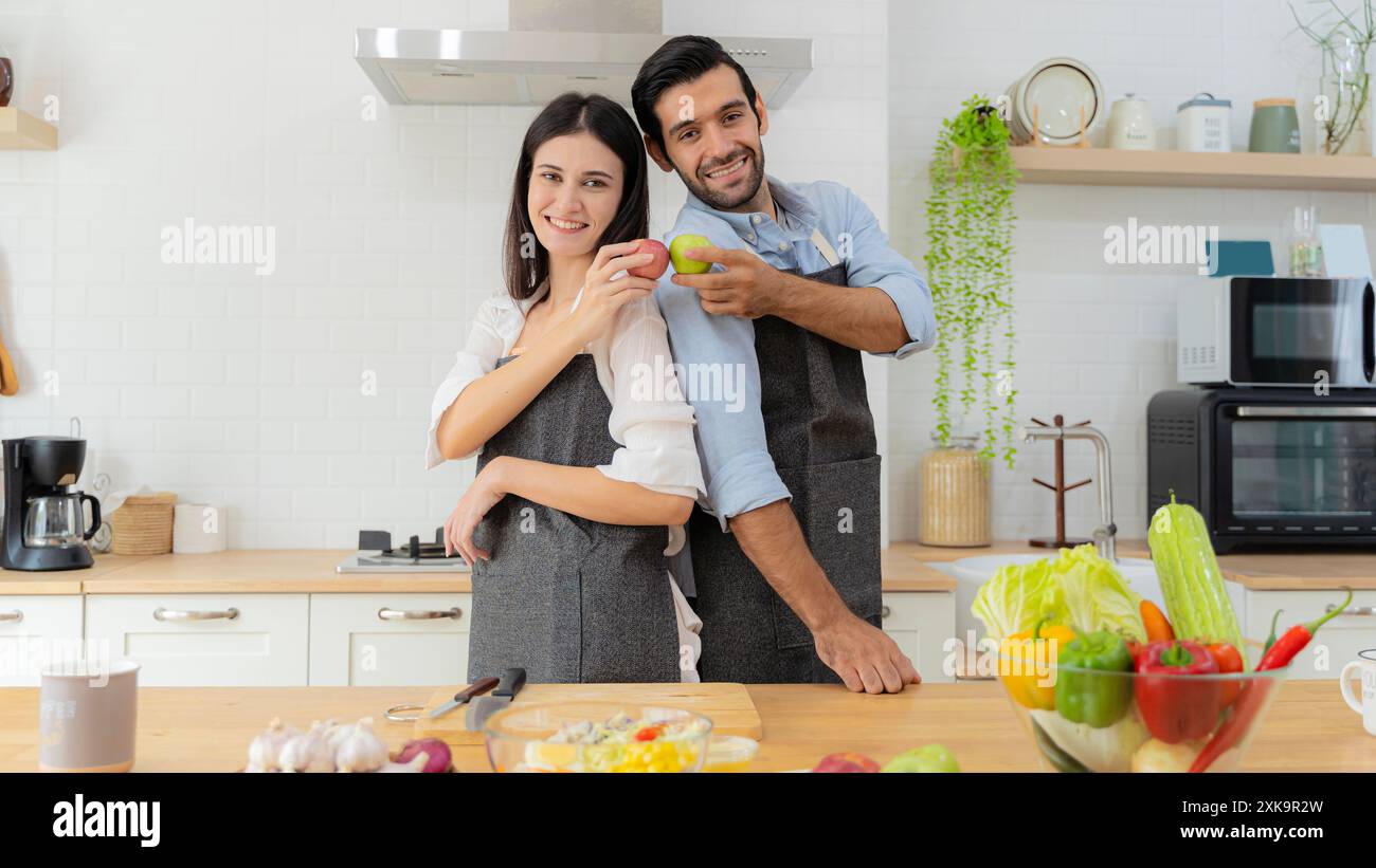 Bella coppia che tiene in mano mele rosse e mele verdi. Una giovane coppia innamorata che si diverte mentre preparano una colazione insieme su un beau Foto Stock