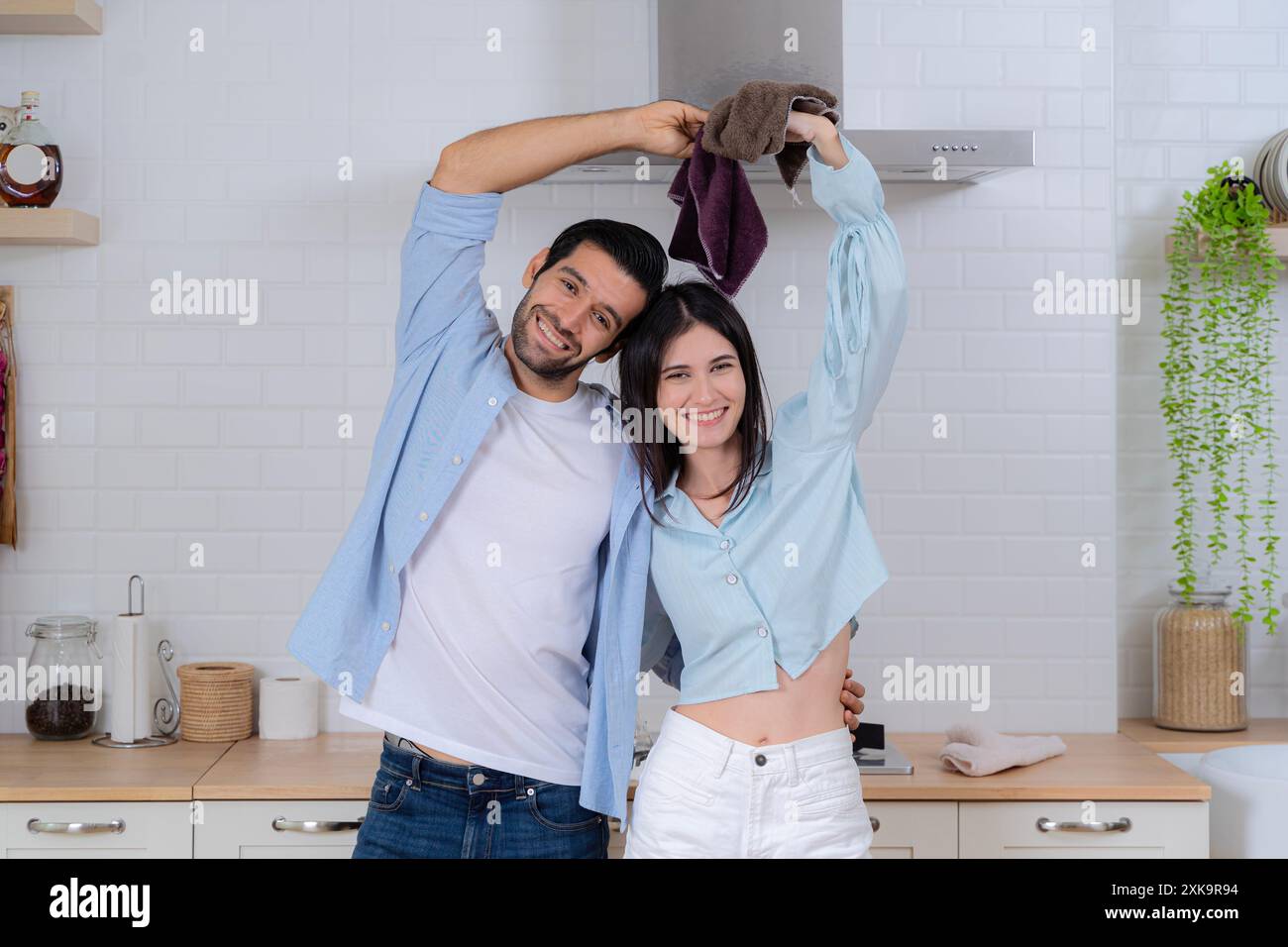 Giovane coppia di famiglia che fa le pulizie in casa. Concetto di pulizia. Allegra giovane signora europea e piatti per il lavaggio degli uomini in un moderno interno della cucina. HY Foto Stock