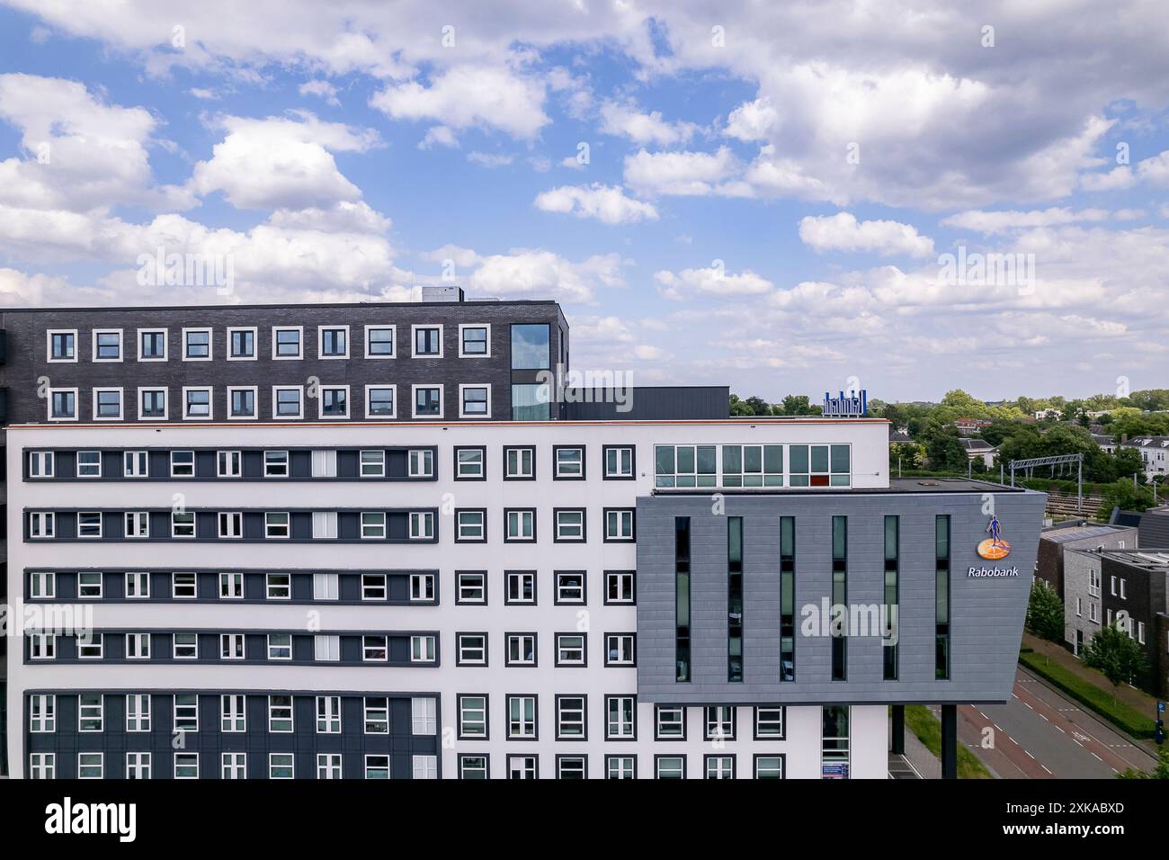 La banca degli agricoltori olandesi Rabobank si innalza sopra le case residenziali all'alba del cielo arancione. Sede di istituti finanziari e di imprese immobiliari Foto Stock