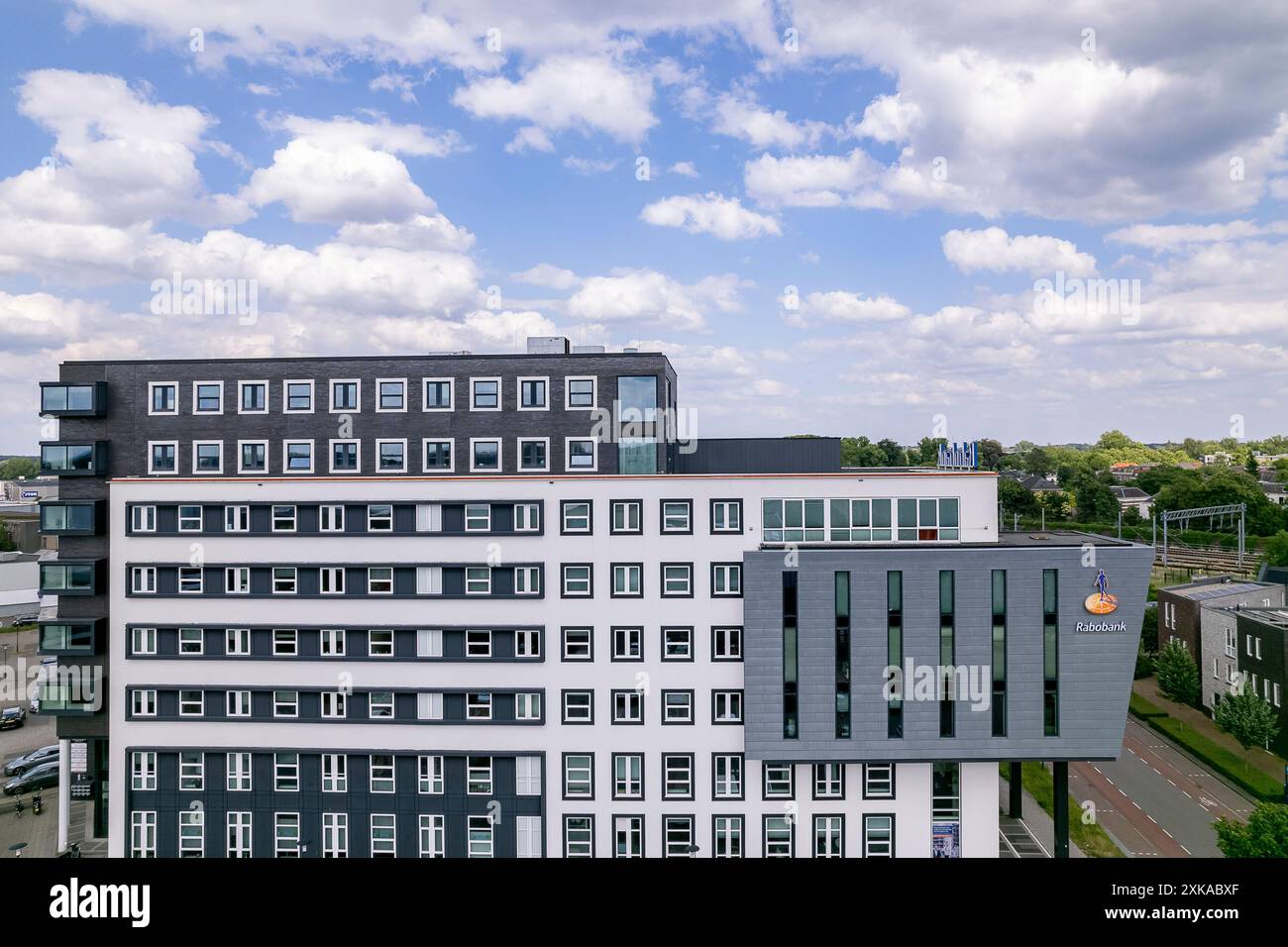 La banca degli agricoltori olandesi Rabobank si innalza sopra le case residenziali all'alba del cielo arancione. Sede di istituti finanziari e di imprese immobiliari Foto Stock