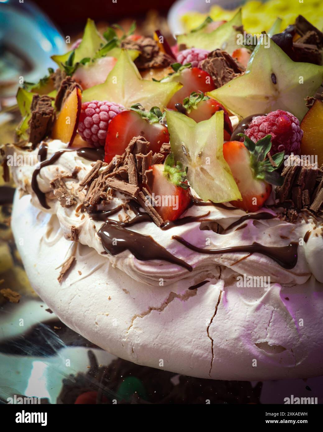 Primo piano di un dessert pavlova condito con frutta fresca, tra cui fragole, lamponi, frutta stellata e scaglie di cioccolato. Foto Stock