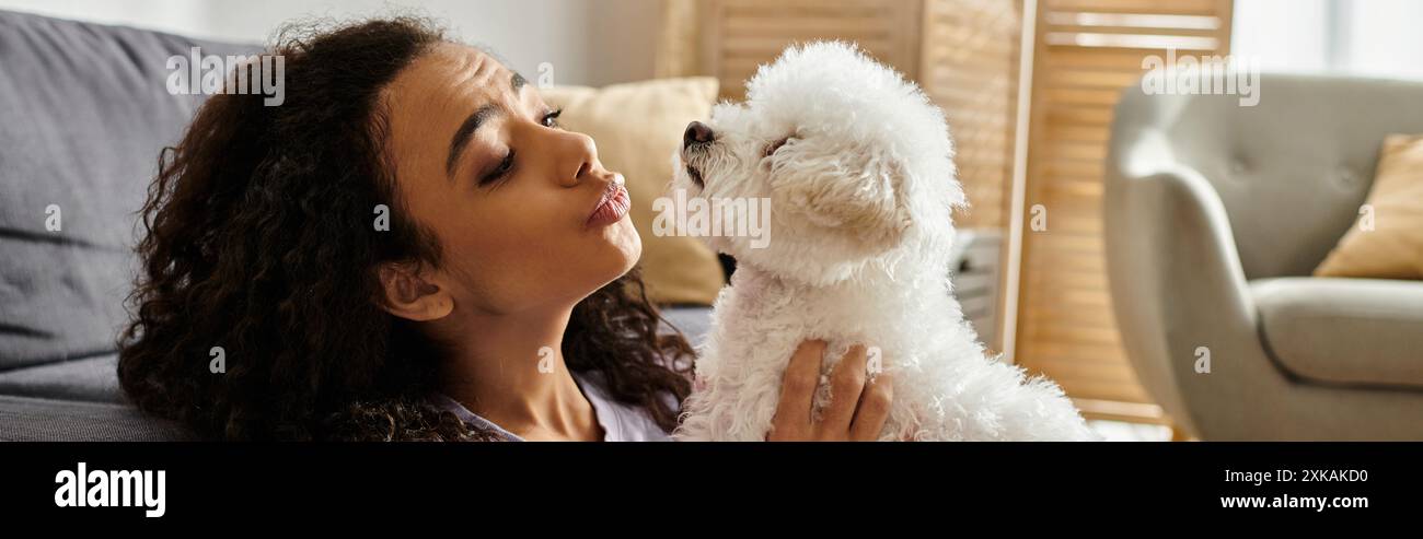 Donna seduta sul divano, tenendo tenero il cane in un ambiente accogliente. Foto Stock