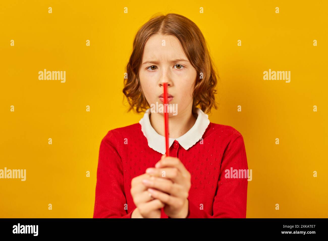 Studentessa adolescente che tiene la matita rossa verticalmente davanti al naso su sfondo giallo Foto Stock