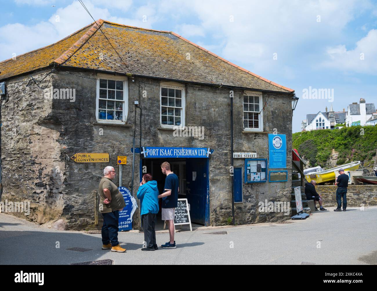 Un trio di persone è in conversazione fuori Port Isaac Fishermen Ltd, un mercato ittico cooperativo sul fronte del porto di Port Isaac, Cornovaglia, Inghilterra, Regno Unito Foto Stock