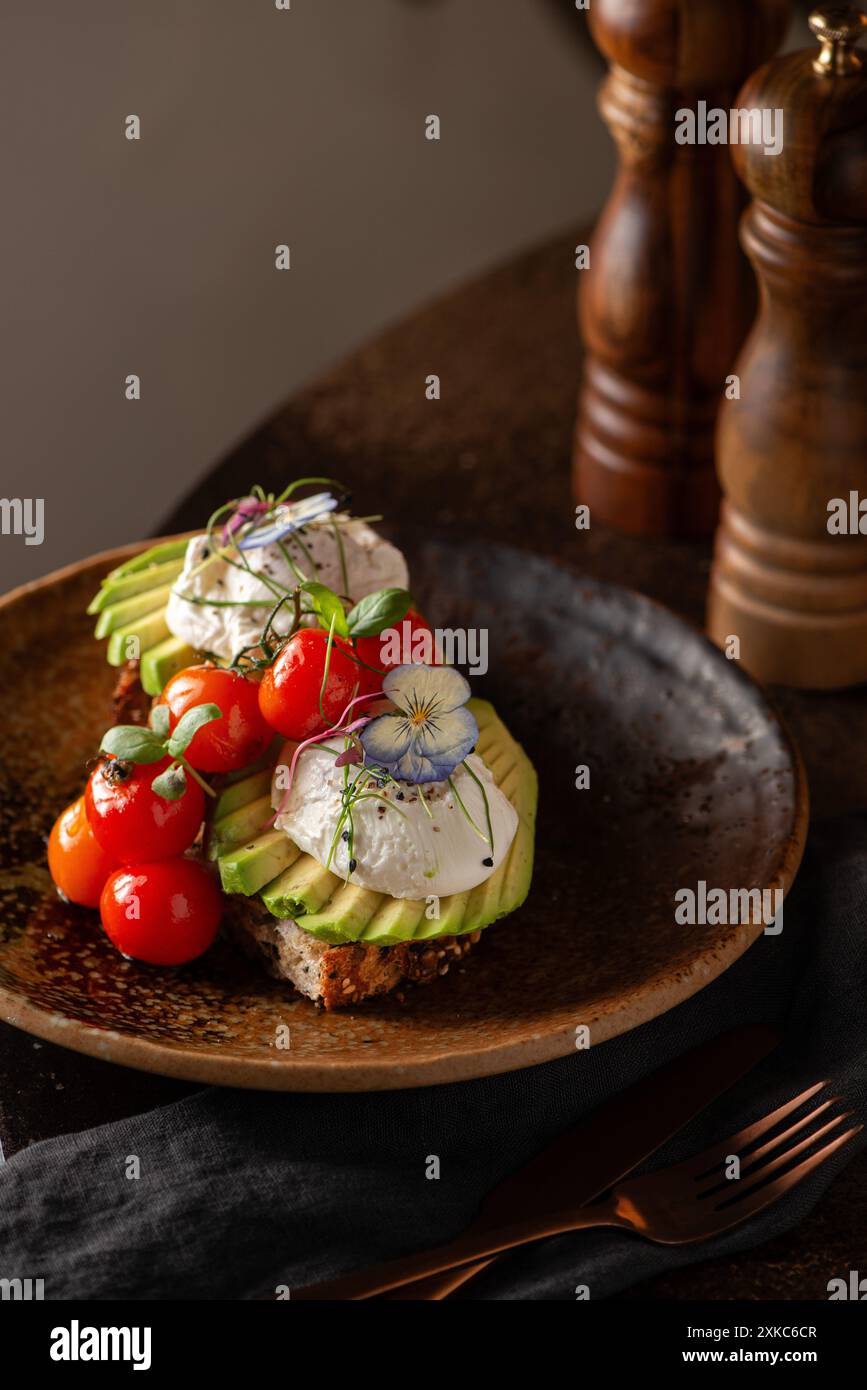 Fetta di pane con avocado a fette, pomodori e uova in camicia. Tavolo del ristorante. Toast a lievito naturale. Foto Stock