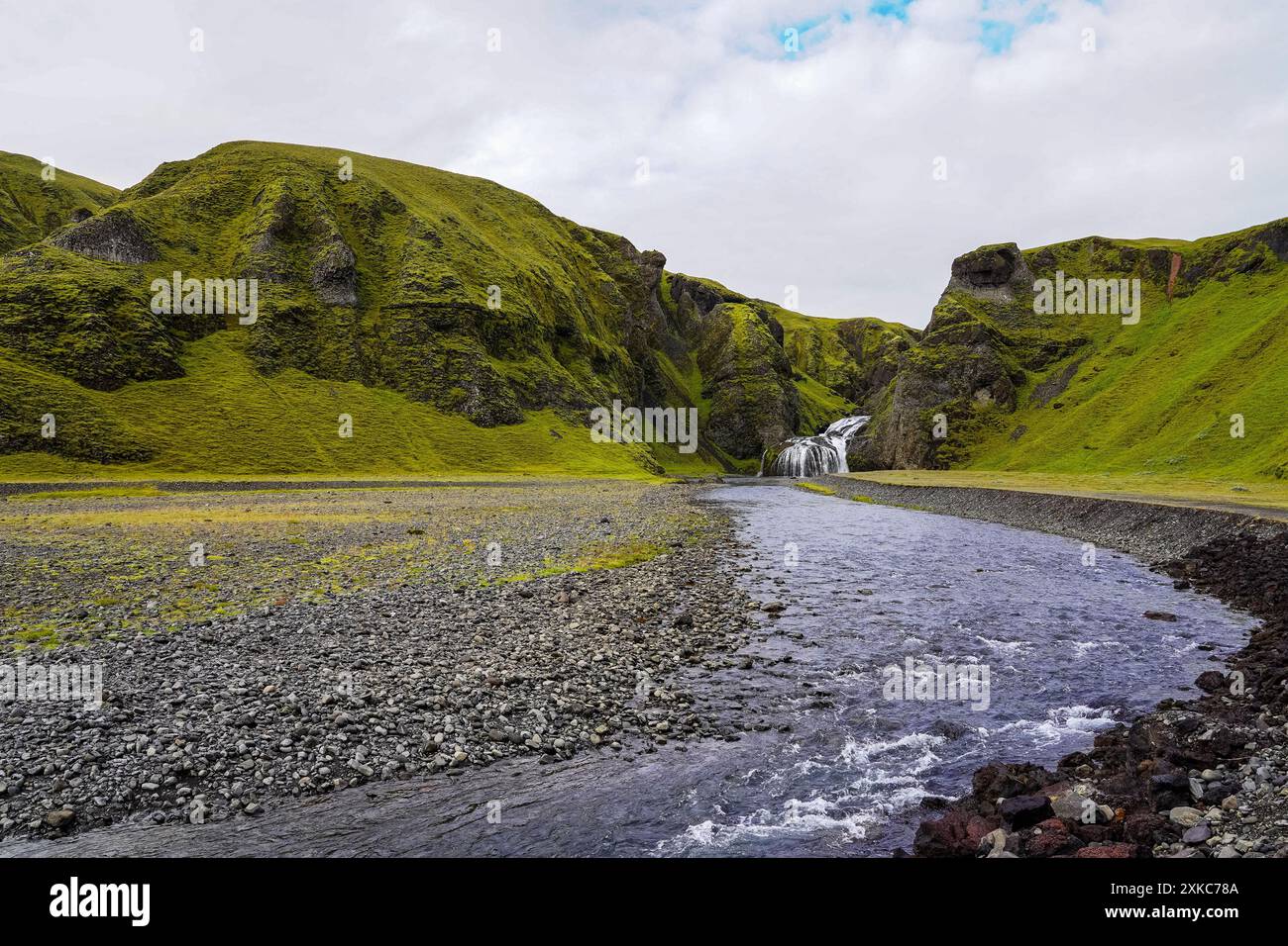 Le cascate panoramiche fluiscono attraverso terreni rocciosi e montagne coperte di muschio sullo sfondo dell'Islanda in un giorno d'estate nuvoloso Foto Stock