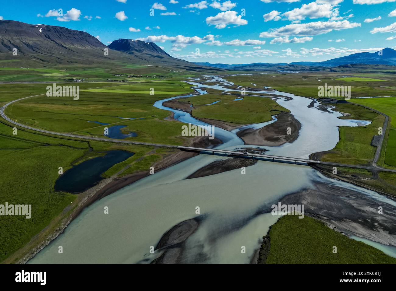 Veduta aerea della strada erbosa della valle attraverso il fiume con ponte vicino alle montagne in Islanda nelle giornate limpide Foto Stock