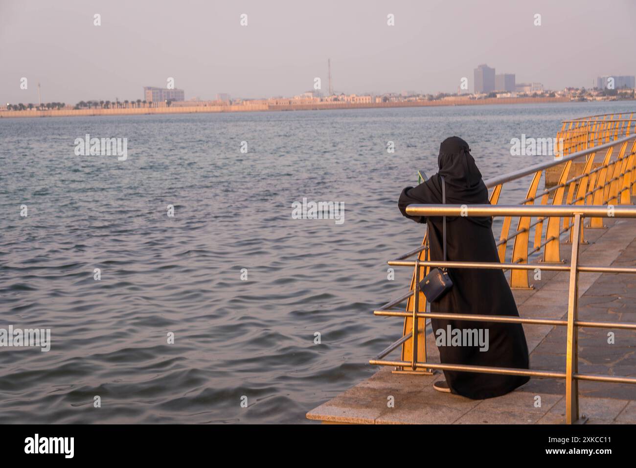 La paranja copriva la donna musulmana sulla Jeddah Corniche (lungomare) in Arabia Saudita che guardava il bellissimo tramonto in Medio Oriente. Foto Stock