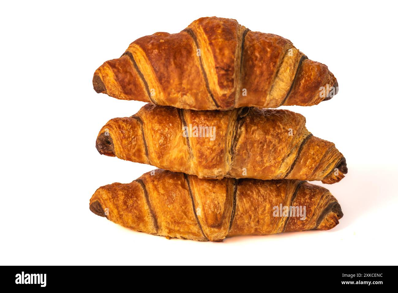 Un trio di croissant perfettamente cotti, marrone dorato e scaglie, sono impilati su uno sfondo bianco. I croissant hanno una leggera lucentezza e strati visibili Foto Stock