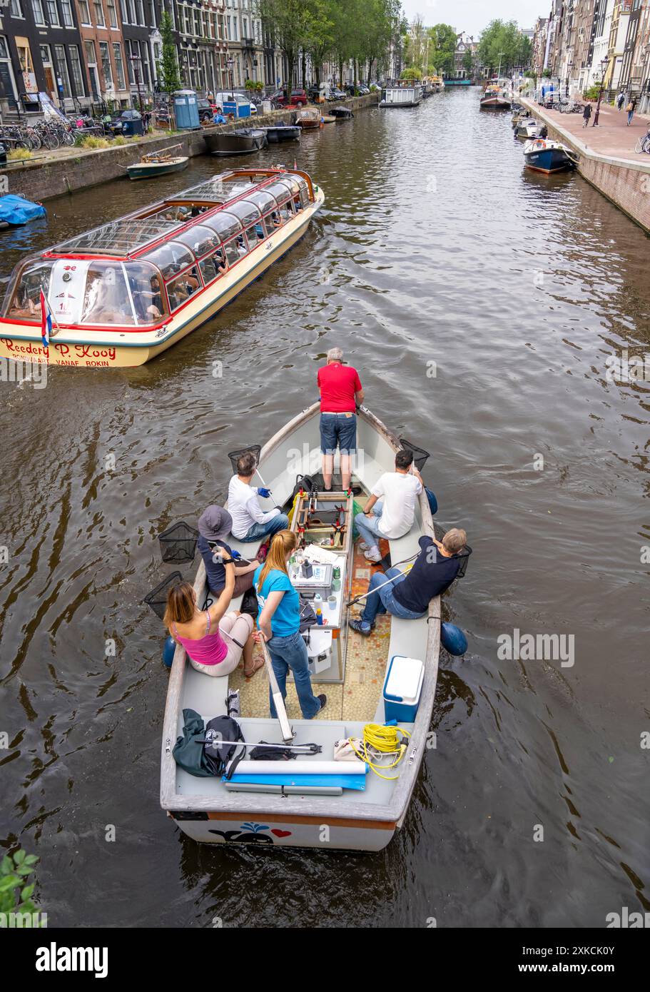 Barca con balena in plastica in un canale di Amsterdam, passeggeri che pescano rifiuti di plastica dai canali, tour attraverso i canali di Amsterdam, raccolta rifiuti A. Foto Stock