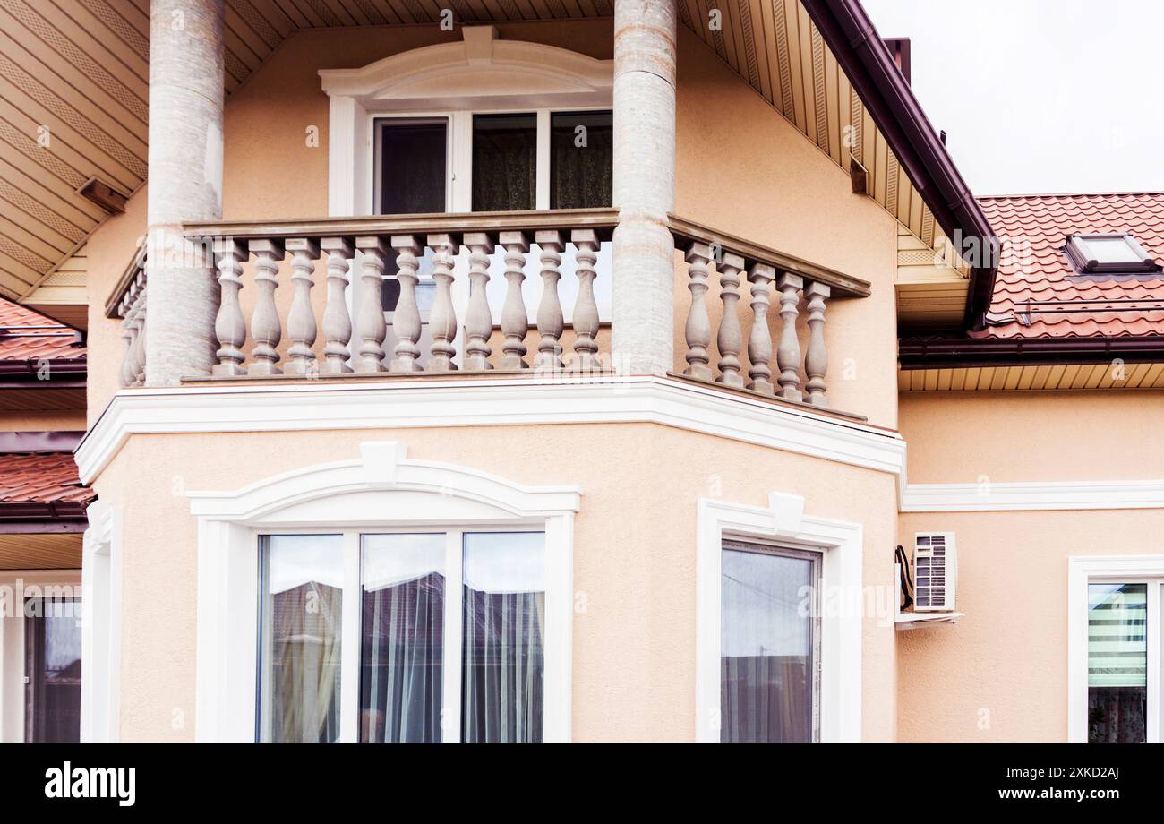 L'esterno di una casa presenta un balcone con balaustre e colonne classiche, pareti beige e tegole rosse. Foto Stock