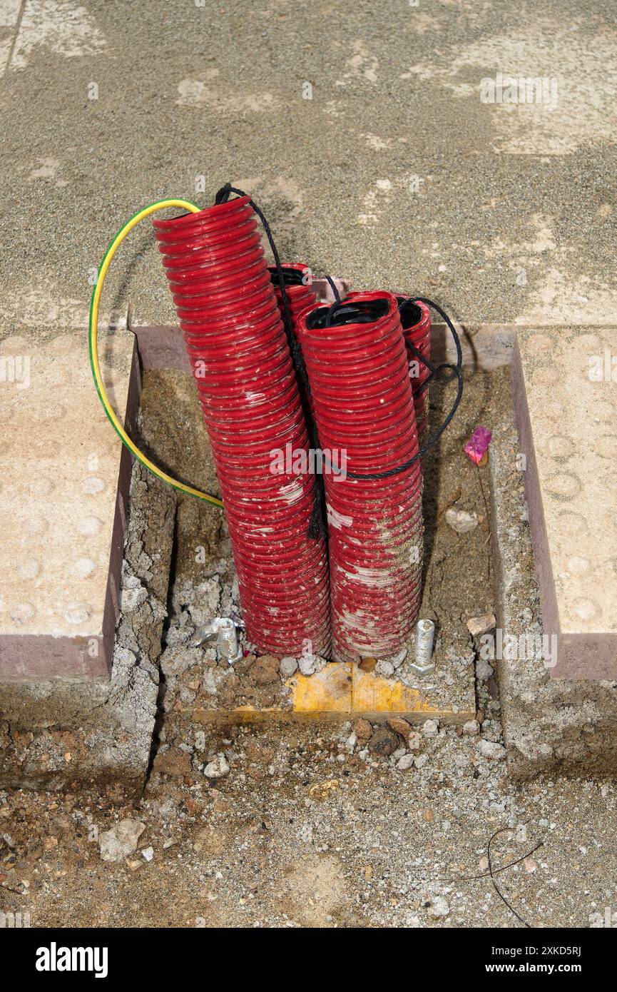 Immagine di due tubi corrugati rossi legati insieme in una struttura in cemento, con un cavo giallo avvolto intorno a uno di essi, in un ambiente di costruzione. Foto Stock