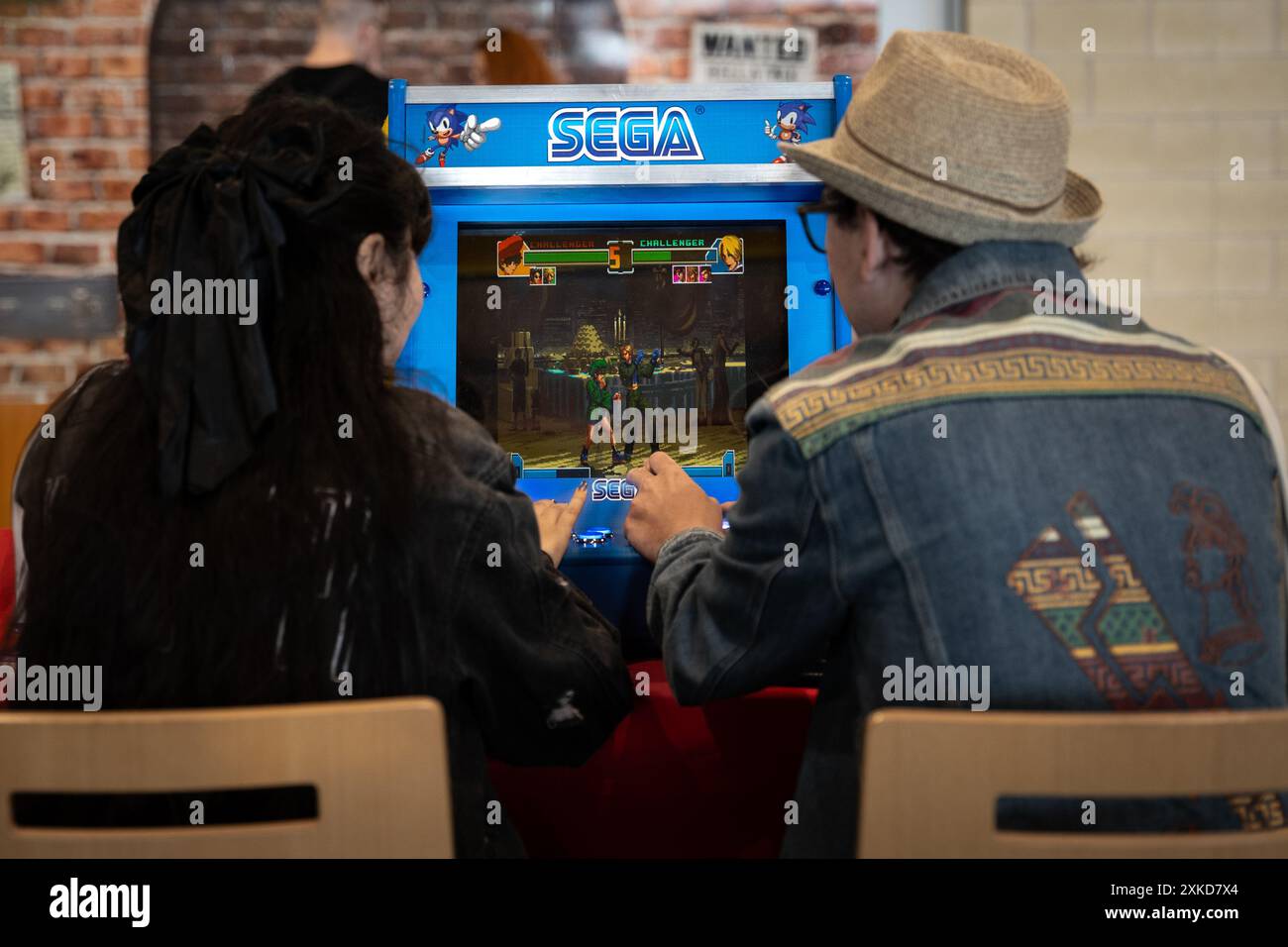 HARROGATE, REGNO UNITO - 22 GIUGNO 2024. Vista posteriore di due amici che giocano uno contro l'altro in un gioco arcade sega retrò durante un evento videoludico Foto Stock