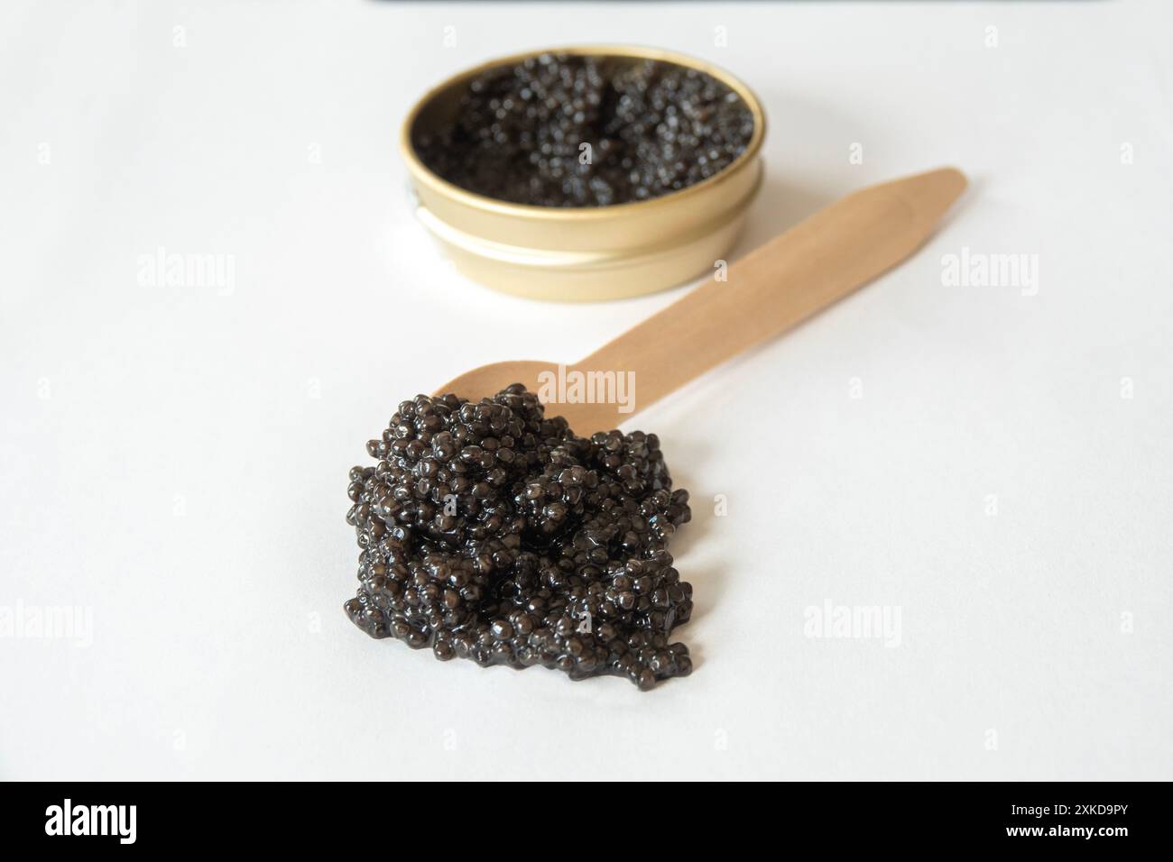 Caviale nero con cucchiaio e barattolo aperto sfocato su sfondo bianco. Vista dall'alto. Prelibatezze di pesce gourmet. Foto Stock