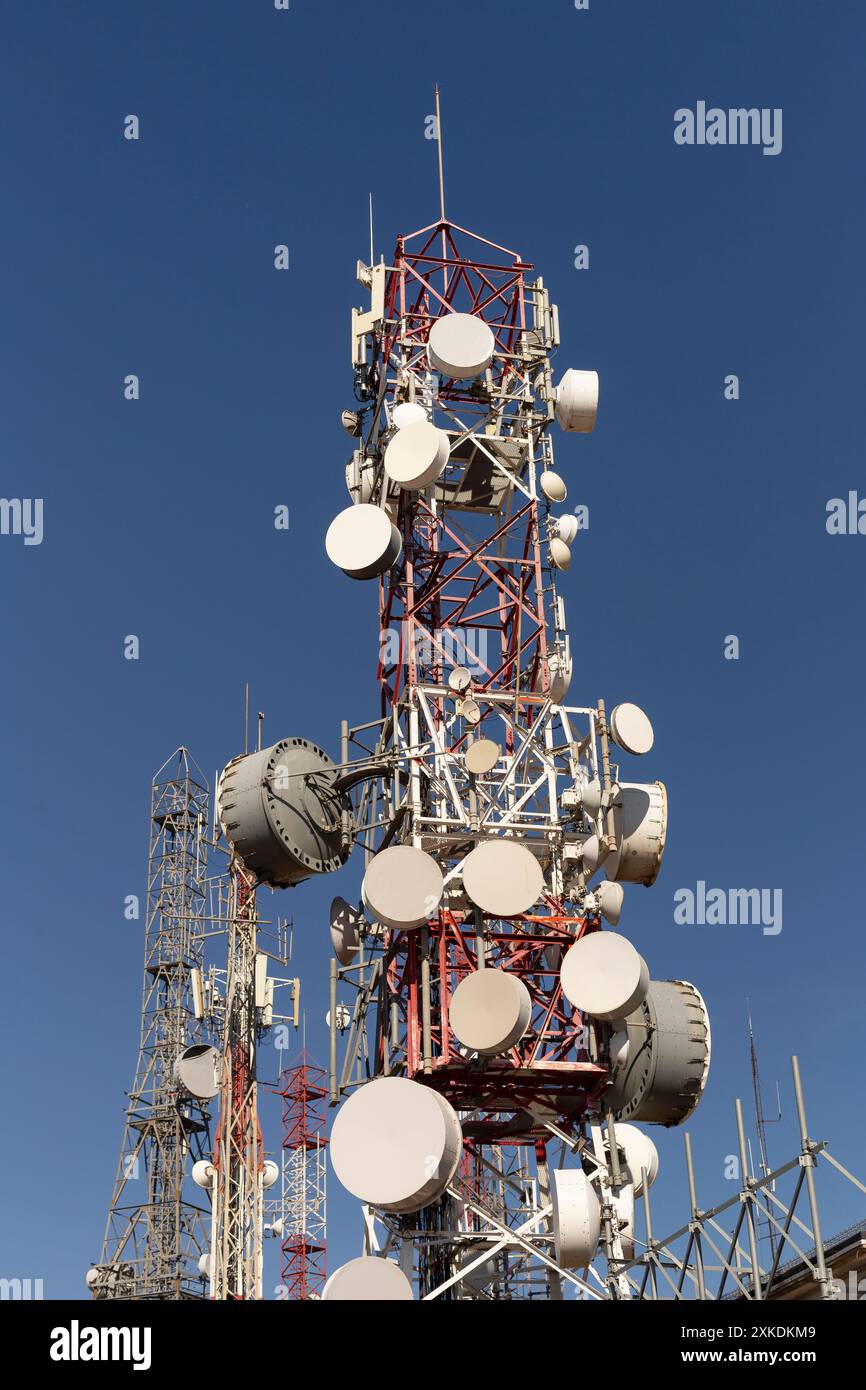 Un'alta torre di comunicazione con molte antenne in cima. La torre è circondata da altre torri. Il cielo è limpido e blu. Foto Stock