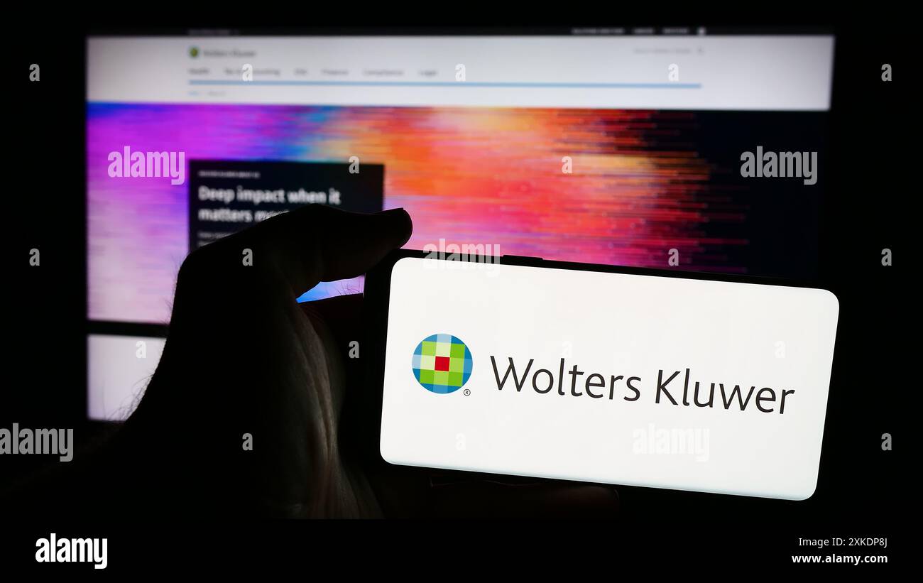 Persona che possiede uno smartphone con il logo della società olandese di servizi di informazione Wolters Kluwer N.V. davanti al sito web. Mettere a fuoco il display del telefono. Foto Stock