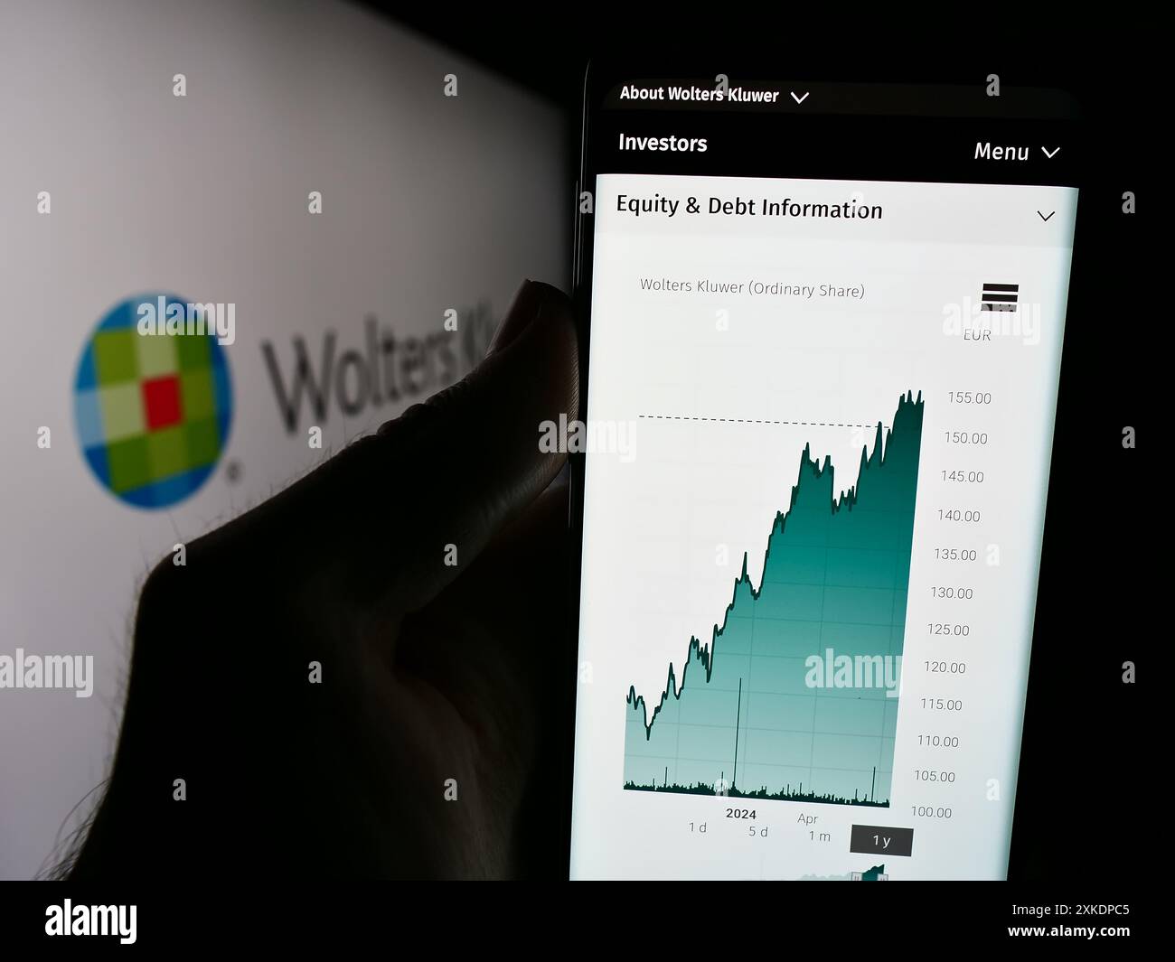 Persona che detiene il cellulare con il sito web della società olandese di servizi d’informazione Wolters Kluwer N.V. con il logo. Messa a fuoco al centro del display del telefono. Foto Stock