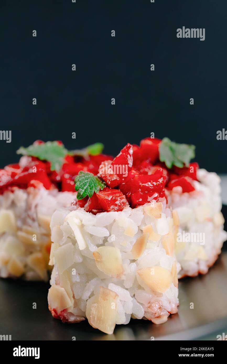 Un moderno sushi roll fusion condito con fragole a dadini e guarnito con foglie verdi su sfondo scuro Foto Stock