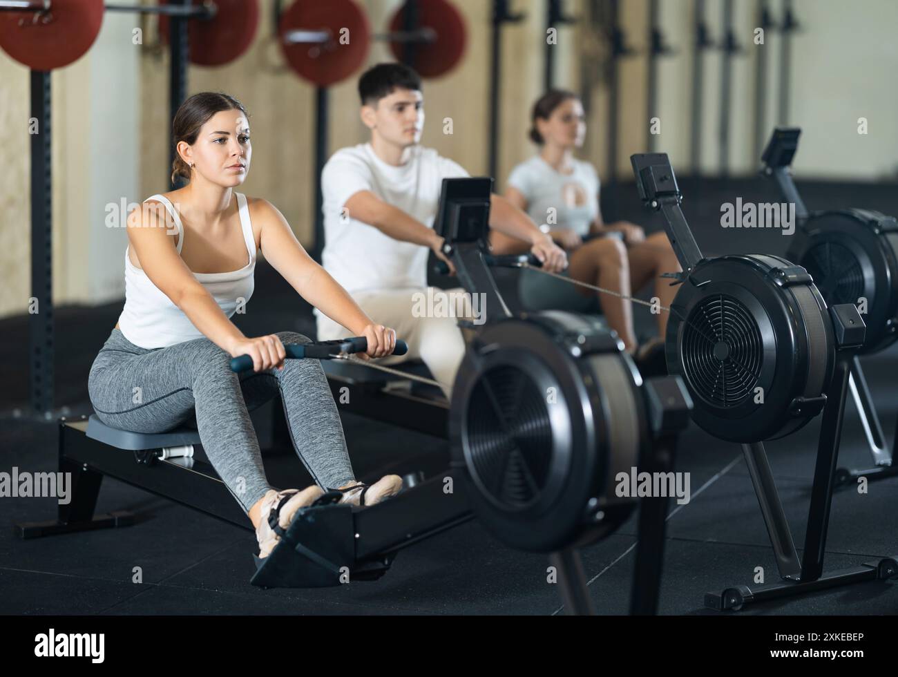 Allenamento femminile cross training esercizio cardio con vogatore con gruppo di persone nel club Foto Stock