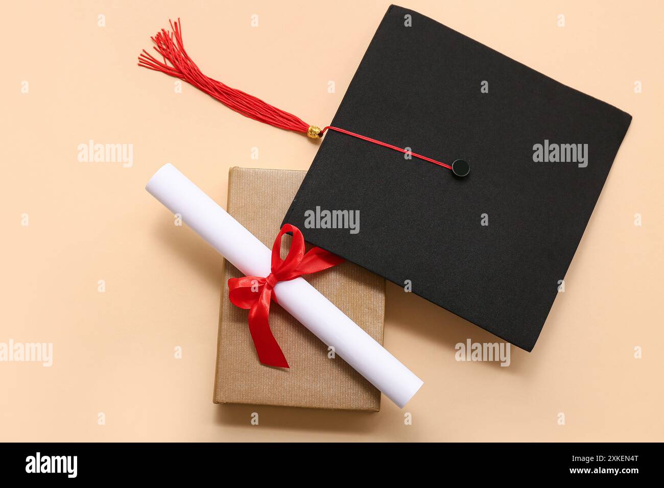 Diploma con nastro rosso, libro e cappello graduato su sfondo beige Foto Stock