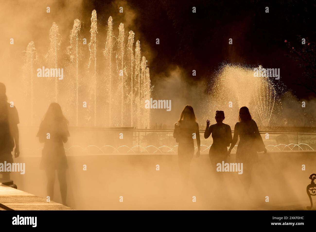 Bucarest, Romania. 22 luglio 2024: La gente cammina attraverso il getto di una fontana in una giornata molto calda. Crediti: Lucian Alecu/Alamy Live News Foto Stock