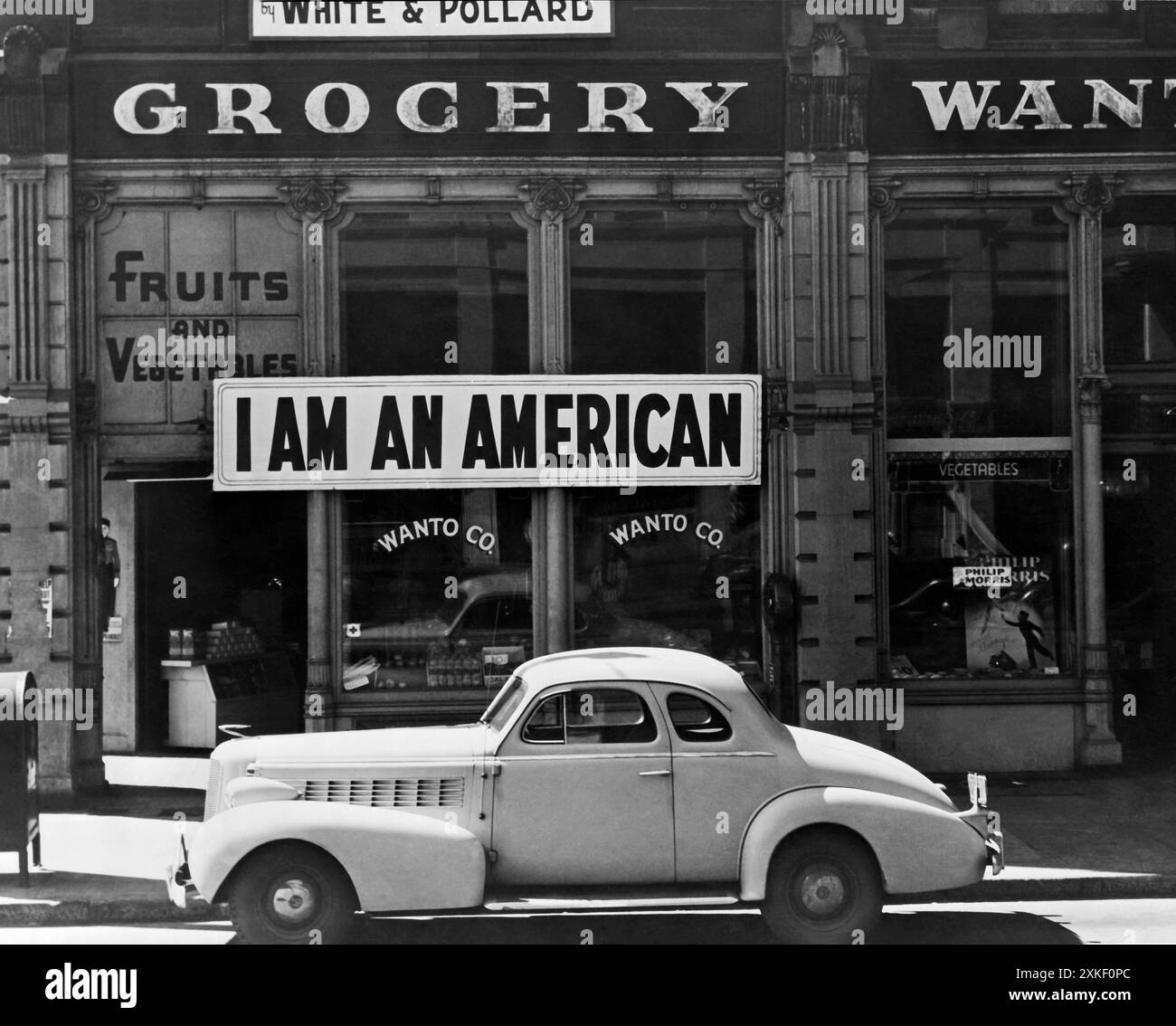 Oakland, California March, 1942 Un grande cartello con la scritta "i am an American" posto nella vetrina di un negozio, a 8th e Franklin Street, l'8 dicembre, il giorno dopo Pearl Harbor. Il negozio è stato chiuso in seguito all'ordine a persone di origine giapponese di evacuare da alcune aree della costa occidentale. Il proprietario, laureato all'Università della California, sarà ospitato con centinaia di sfollati nei centri della War Relocation Authority per tutta la durata della guerra. Foto Stock