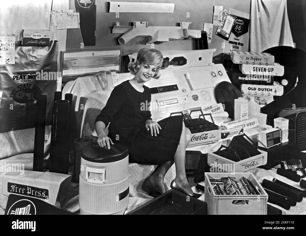 Bartlesville, Oklahoma, 1962 ca. Una donna seduta in una stanza piena di prodotti Phillips Petroleum che vanno dall'involucro congelatore alle materie plastiche di tutti i tipi. Foto Stock