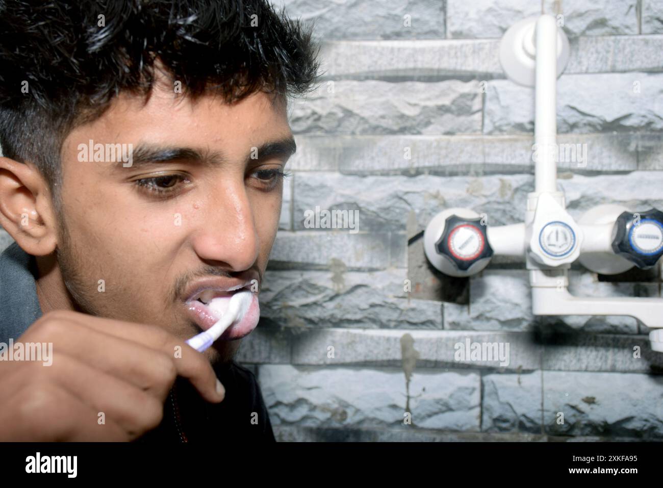 Un ragazzo che spazzolava i denti in bagno, camicia nera Foto Stock