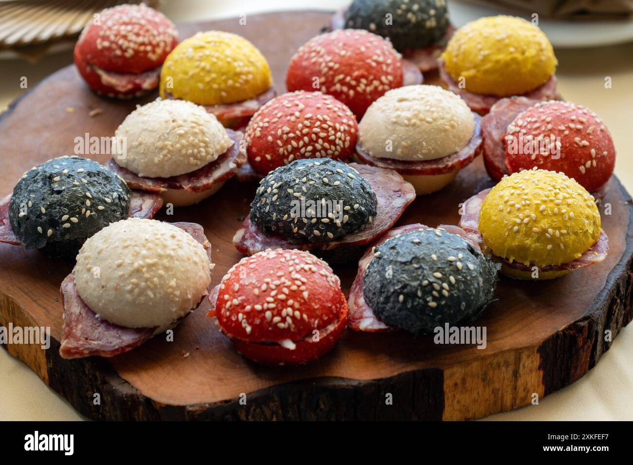 Piccoli e gustosi panini al salame con panini colorati presentati su un piatto rustico di legno Foto Stock
