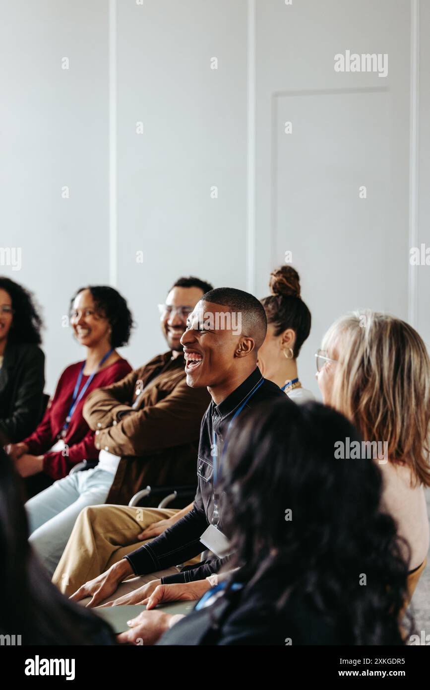 Uomo d'affari che ride in un seminario con un gruppo di persone diverse. Atmosfera positiva e interazione gioiosa durante una riunione d'affari. Foto Stock