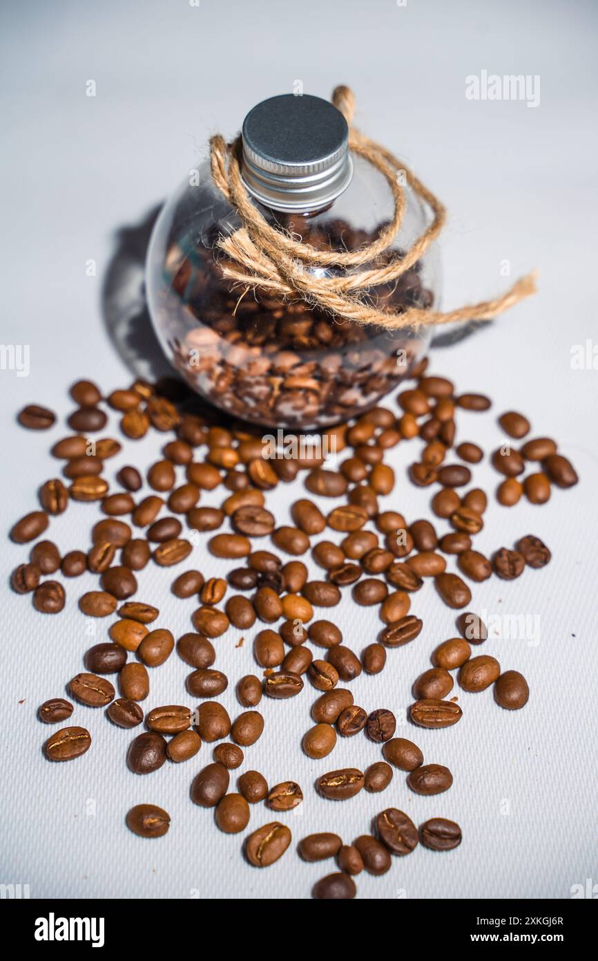 una collezione di chicchi di caffè freschi di colore marrone chiaro che vengono messi in una bottiglia di vetro rotonda chiusa circondata da una spolverata di chicchi di caffè Foto Stock